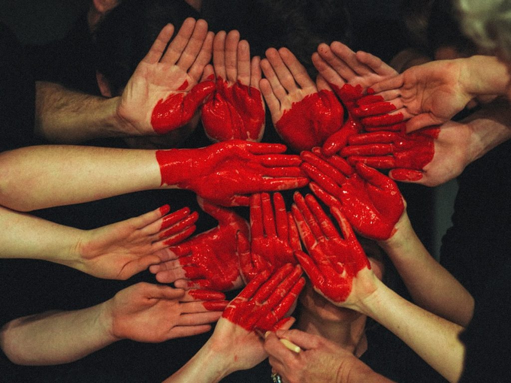 Eine Gruppe von Menschen legen ihre rot gefärbten Hände zu einem Herzen zusammen