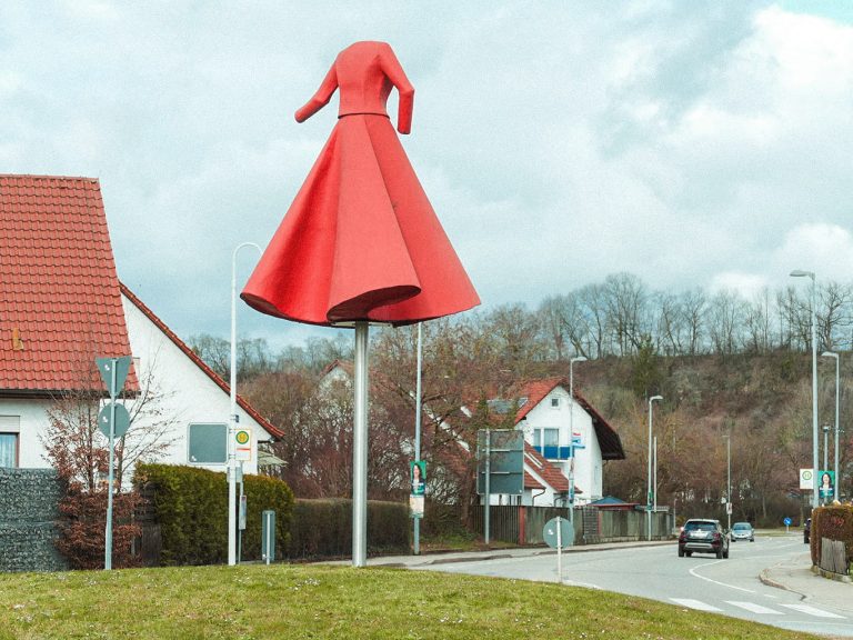 Über einem Kreisverkeht in Eislingen ist die Plastik eines großen roten Kleides angebracht. Im Hintergrund ist eine Landstraße zu sehen
