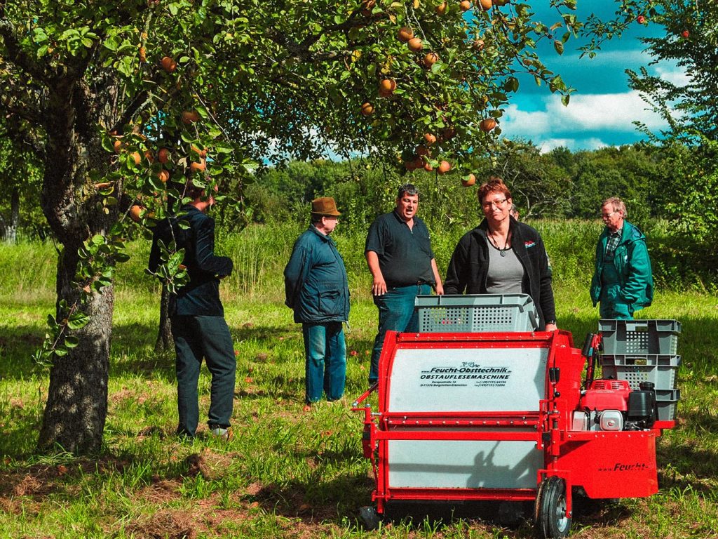Eine Gruppe von Menschen stehen auf einer Streuobstwiese um einer Apfelerntemaschine