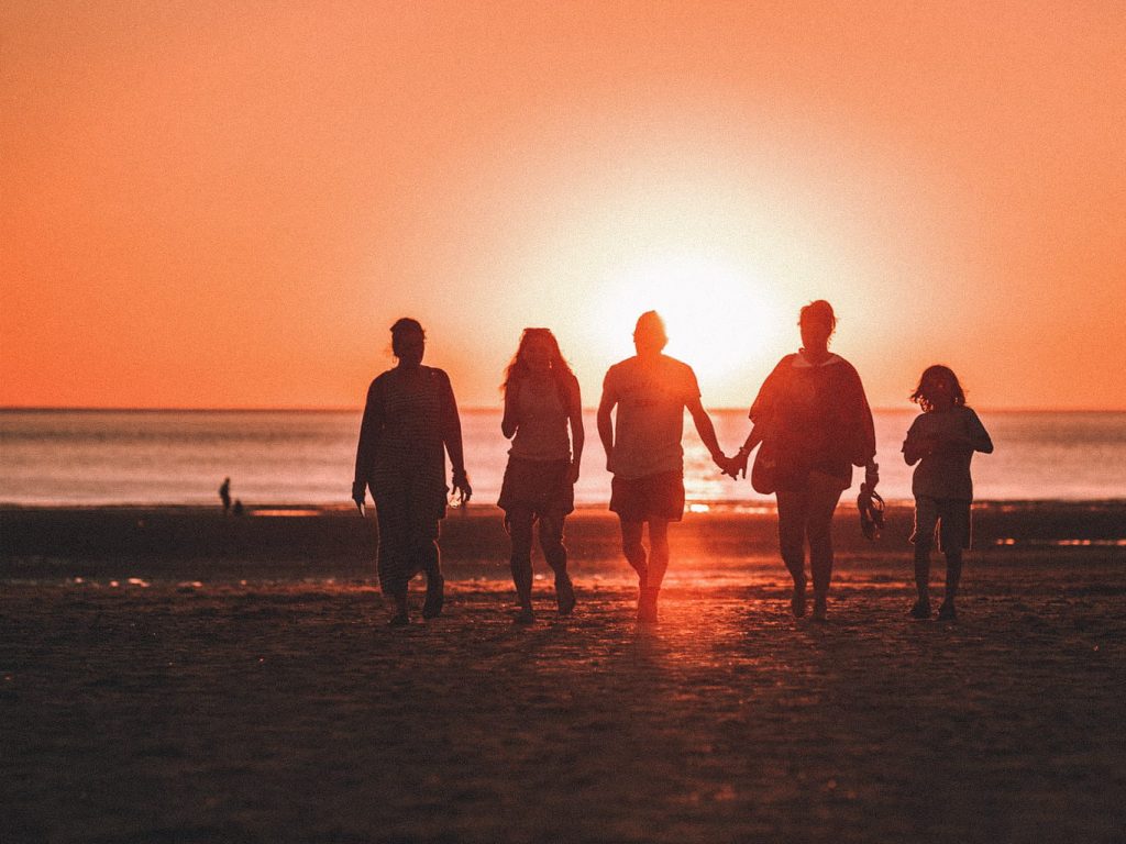 Eine Gruppe von unterschiedlich großen Menschen gehen Hand in Hand bei einem Sonnenuntergang auf dem Strand