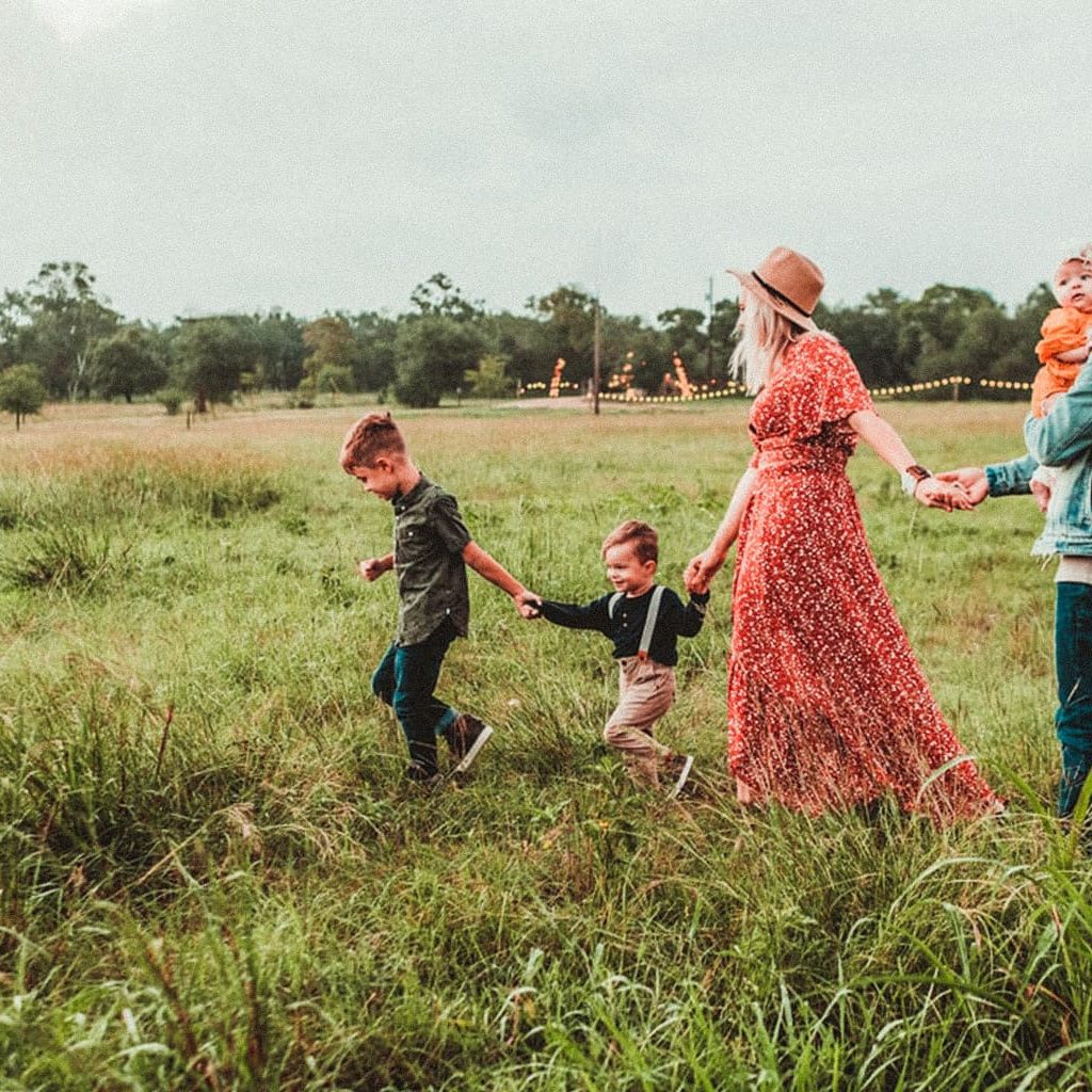 Eine Frau und ein Mann mit drei Kindern spazieren zusammen über ein Feld