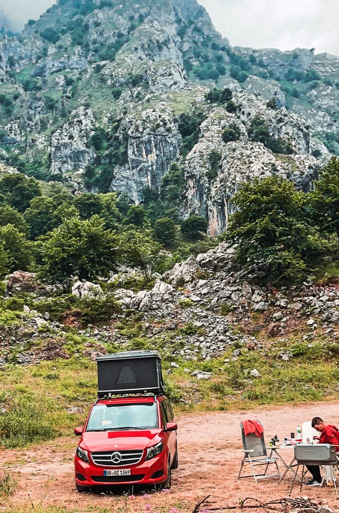 Eine Person sitzt neben einem roten Van vor einer Felswand und berücksichtigt dabei Wohnmobiltipps