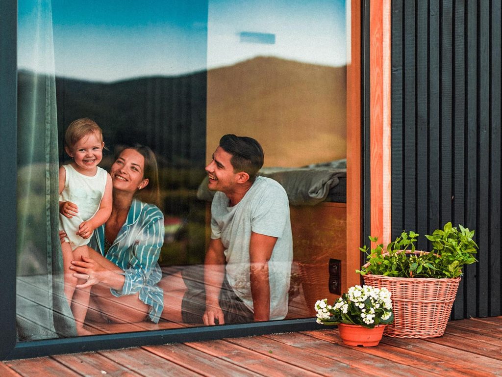 Eine Familie mit Kleinkind sitzt hinter einer Glastür und schaut raus