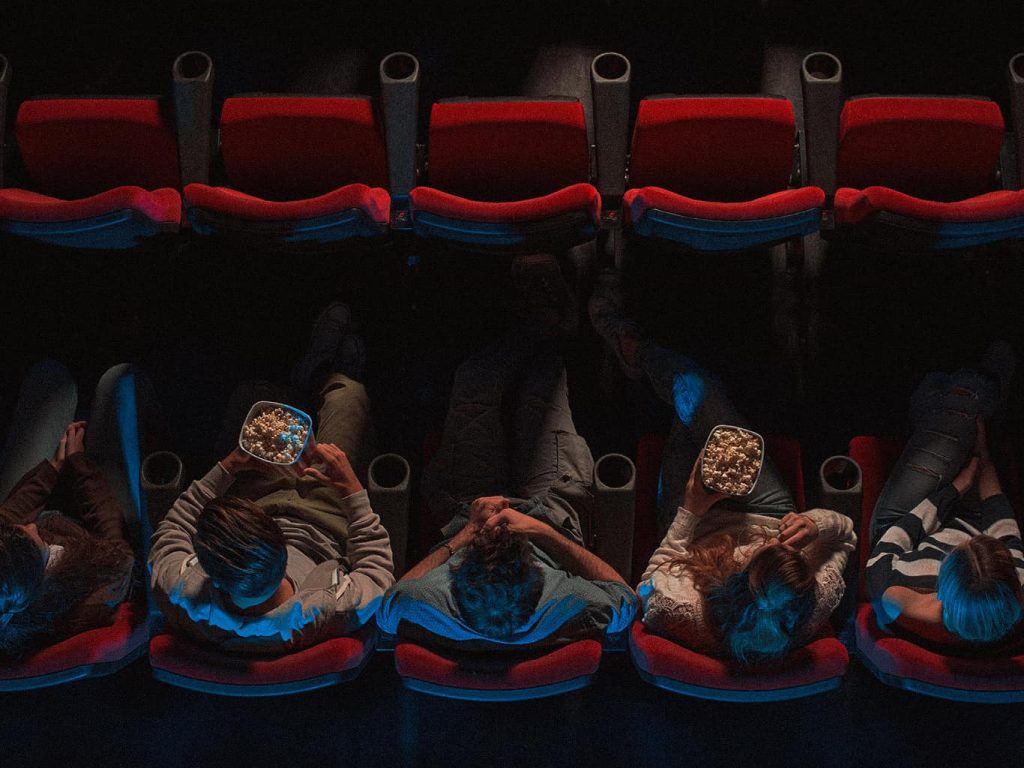 Vier Menschen sitzen im Kinosaal und essen Popcorn