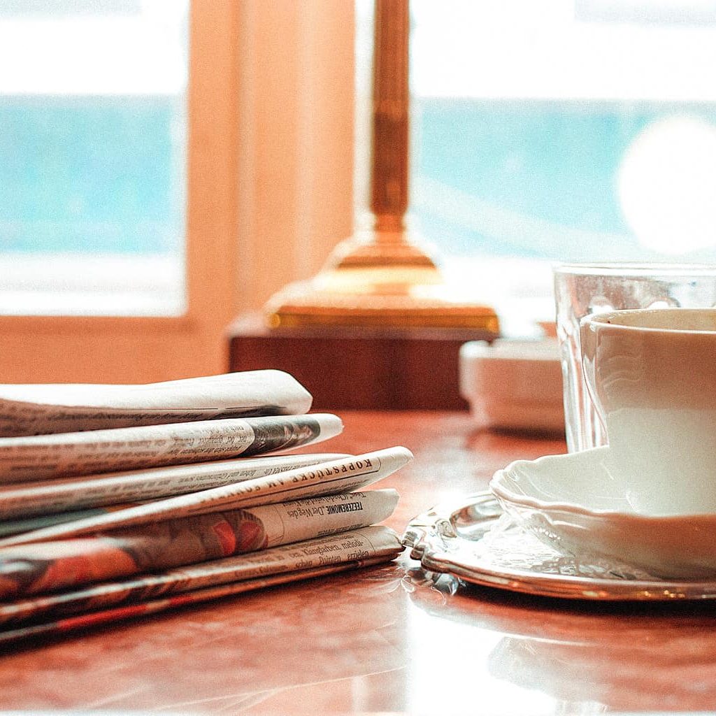 Ein Tisch auf dem Zeitungen sowie ein Kaffee abgestellt sind