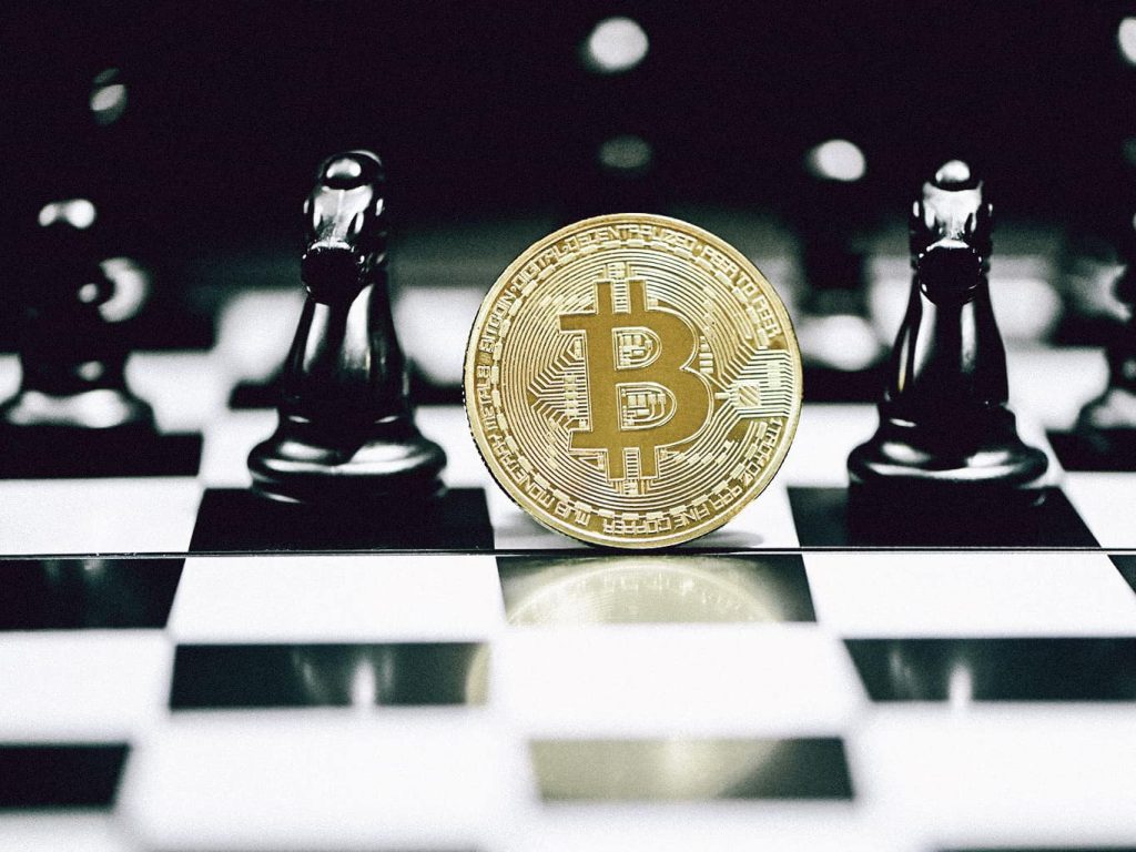 Eine Bitcoin-Münze auf einem Schachbrett, die zwischen zwei Pferde-Schachfiguren steht