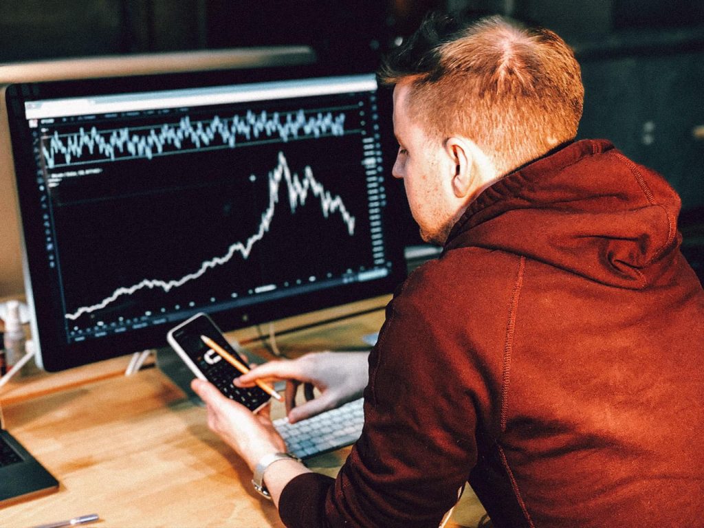Ein Mann kontrolliert auf seinem Smartphone die Aktienkurse des Rechners