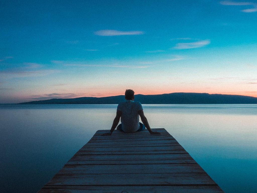 Ein Mann entspannt auf einem Steg vor einem See bei Sonnenuntergang