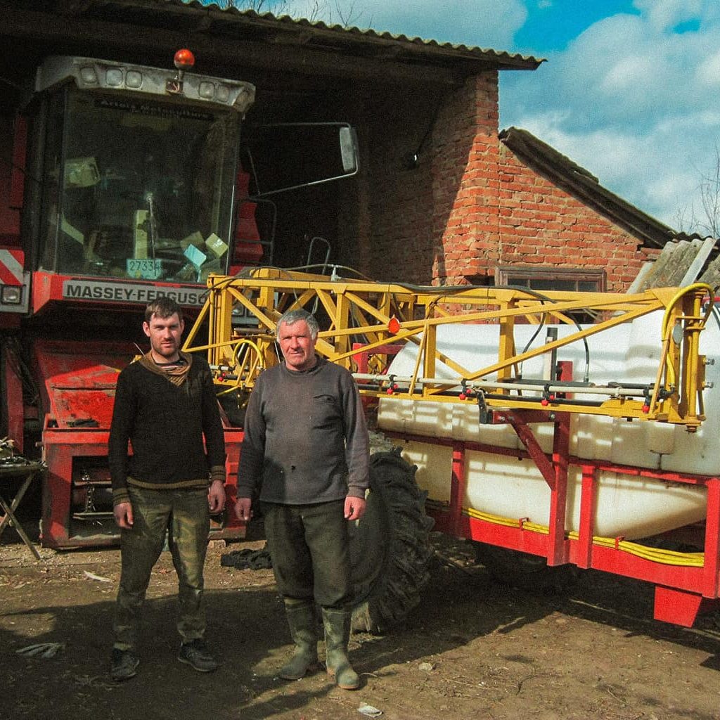 Zwei Männer stehen vor einer großen Landwirtschaftsmaschine, die in einem Schuppen geparkt ist