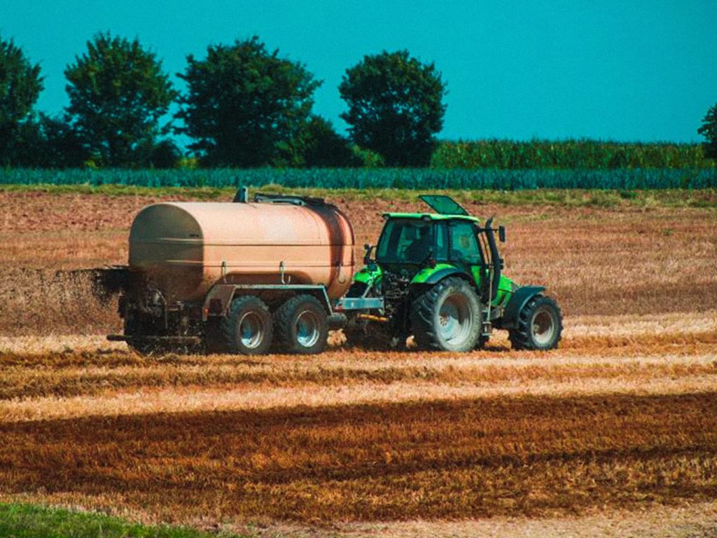 Ein grüner Traktor verteilt auf einem Feld Gülle