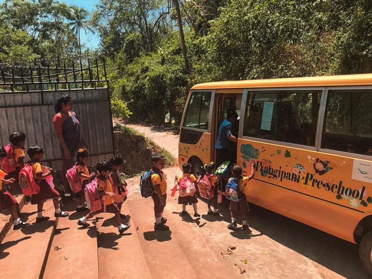Kinder auf einer sandigen Straße in Sri Lanka warten in einer Reihe und steigen in einen gelben Schulbus ein