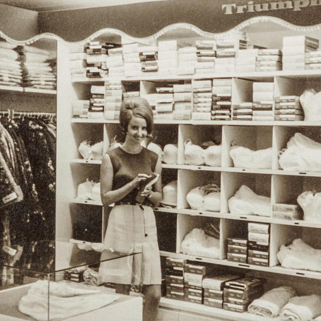 Ein altes schwarz-weiß Foto des Modehauses Frey zeigt eine junge Frau, die vor dem Sortiment steht