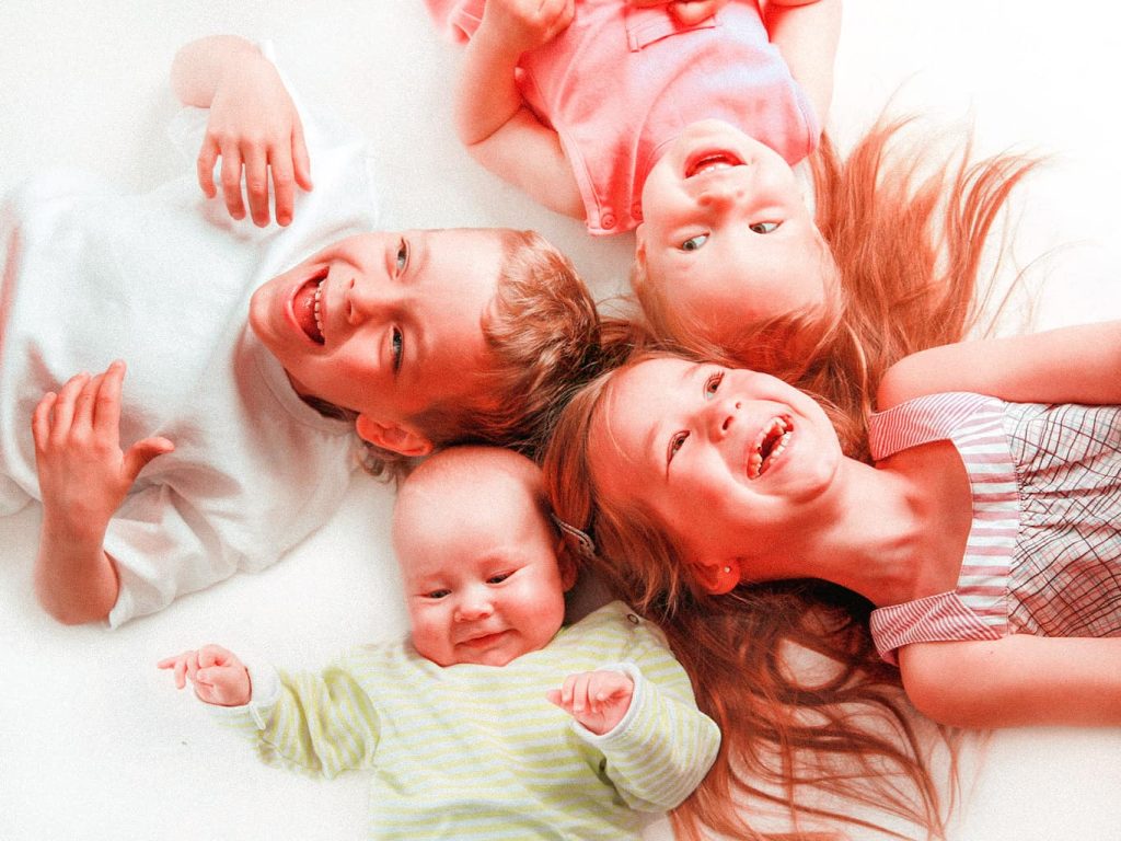 Vier Kinder in unterschiedlichem Alter liegen im Kreis auf dem Boden und lachen