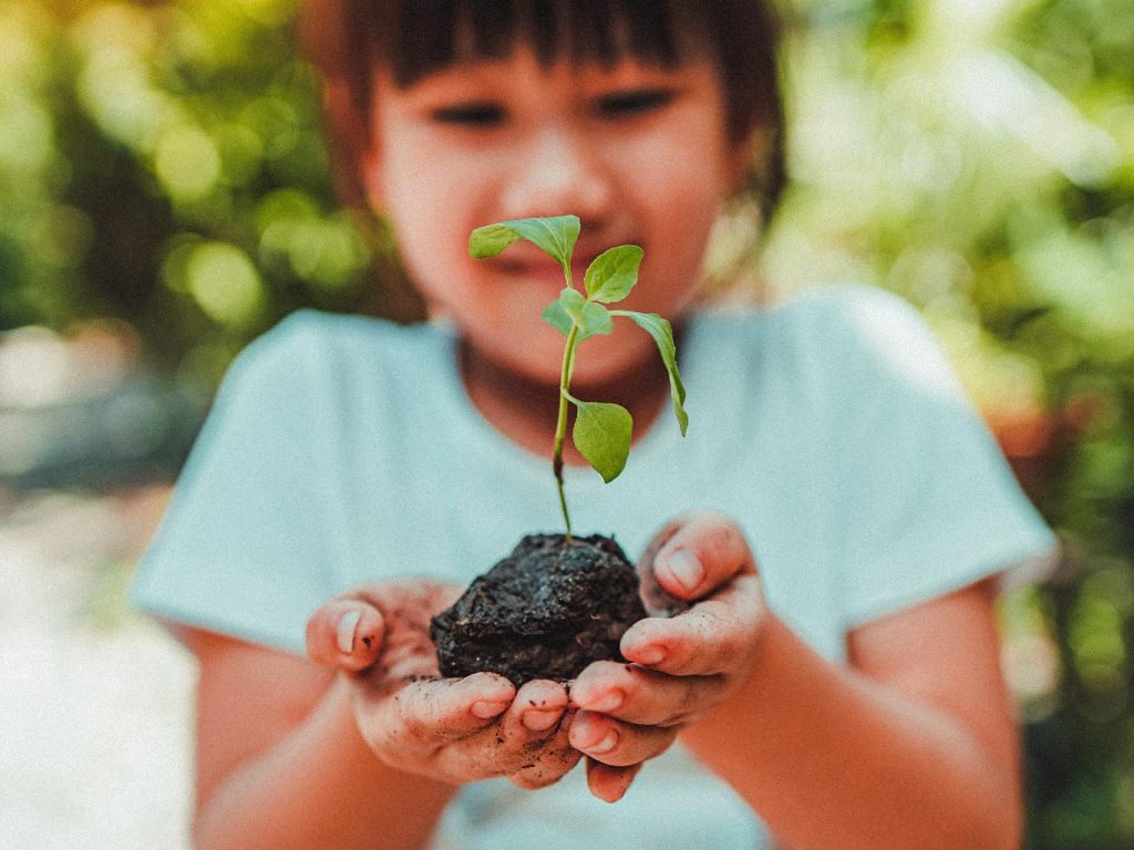 Ein Mädchen hält eine Pflanze mit Erde um den Wurzeln in der Hand