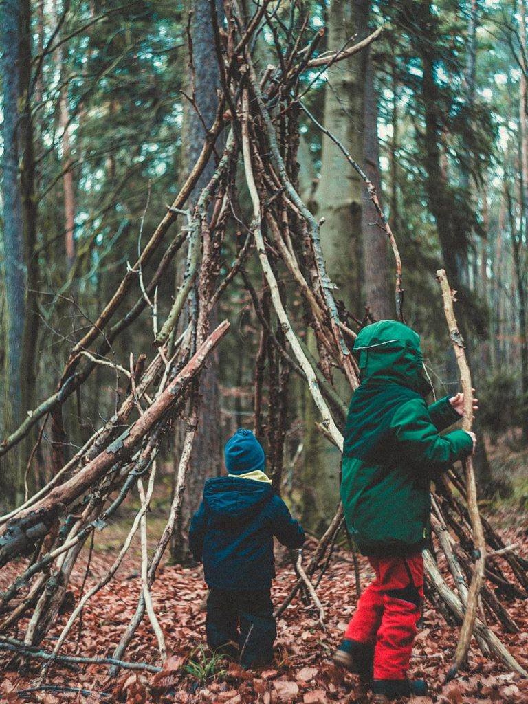 Zwei Kinder bauen ein Zelt aus Stöcken und Ästen im Wald
