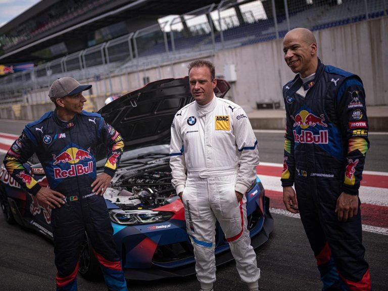 Die Brüder Elias und Johannes Hountondji von den Red Bull Driftbrothers stehen mit einem weiteren Mann in Rennanzug vor einem Wagen des Teams