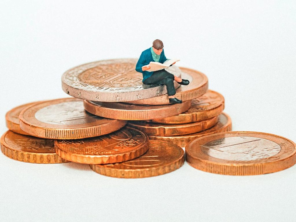 Eine Figur sitzt auf einem Haufen Euromünzen und liest eine Zeitung