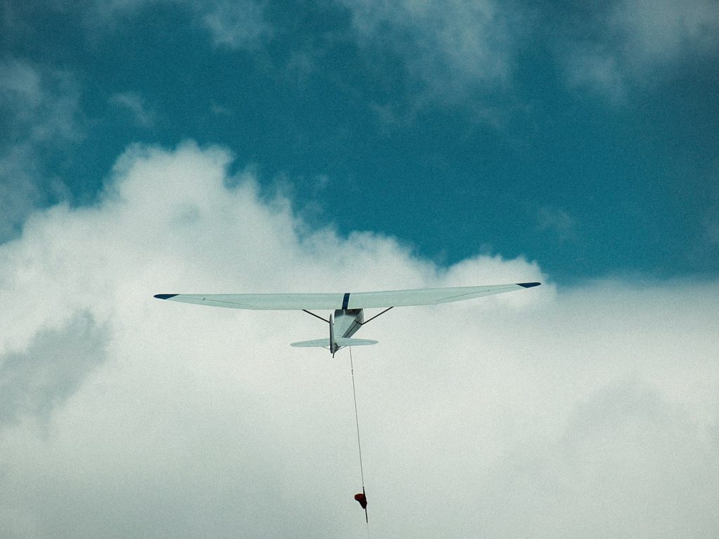Ein Segelflieger schwebt in der Luft, im Hintergrund Wolken im blauen Himmel
