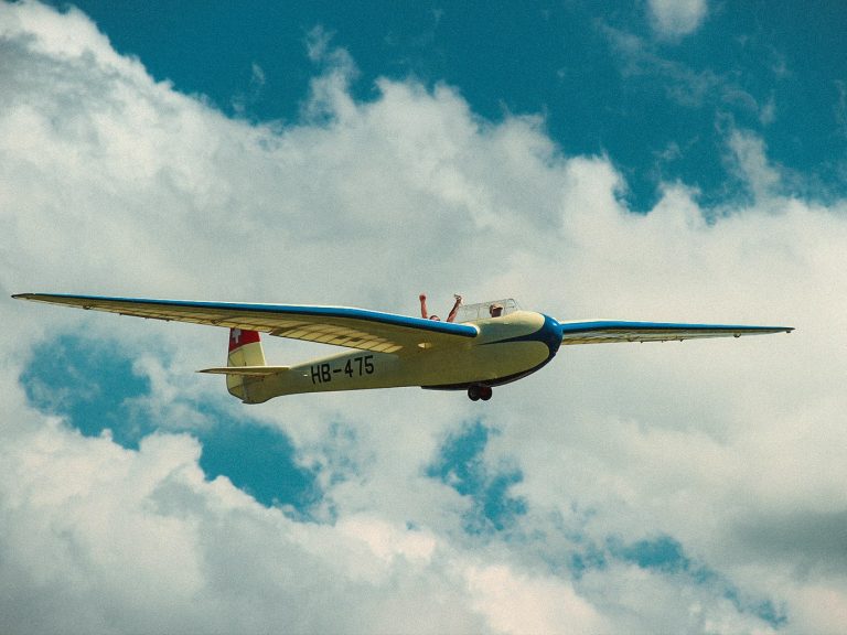 Ein Segelflieger schwebt in der Luft, während ein Insasse des Fliegers seine Hände in die Luft reckt.