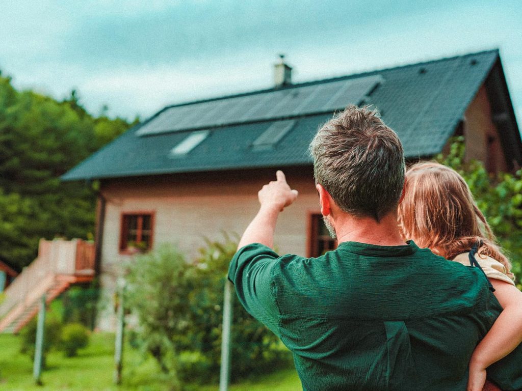 Ein Vater zeigt seiner Tochter, die er in den Armen hält, die Photovoltaikanlage auf dem Dach eines Hauses