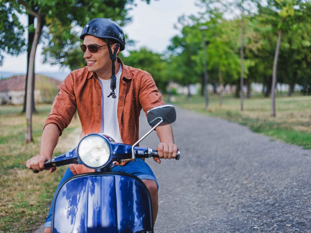 Ein Mann sitzt auf einem blauen Moped und schaut in die Landschaft
