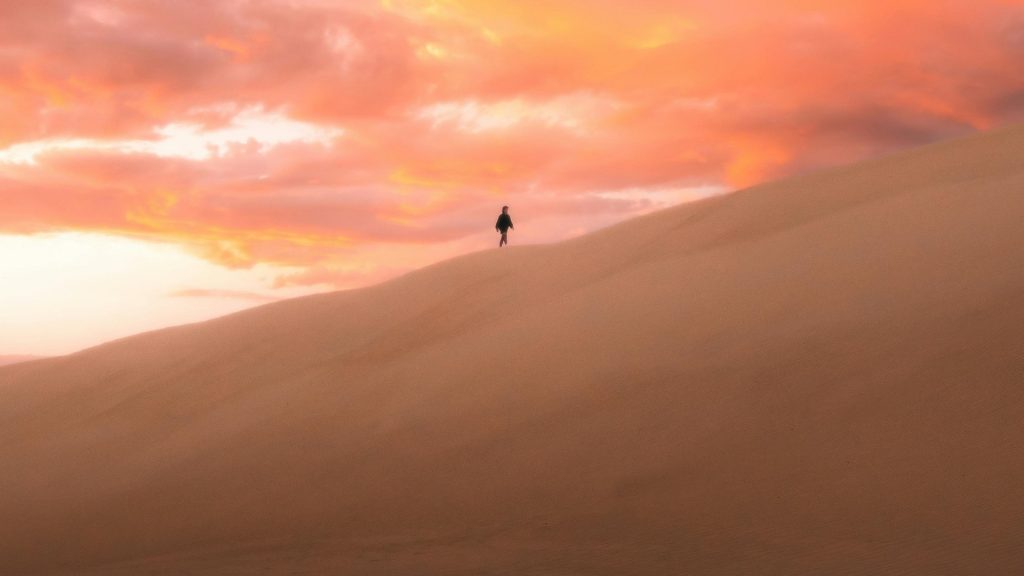 „Samtig & Weich Sparkasse“ – Symbolbild für Wärme, Nähe und Wandel: Person auf Sanddüne vor peachfarbenem Himmel bei Sonnenuntergang.