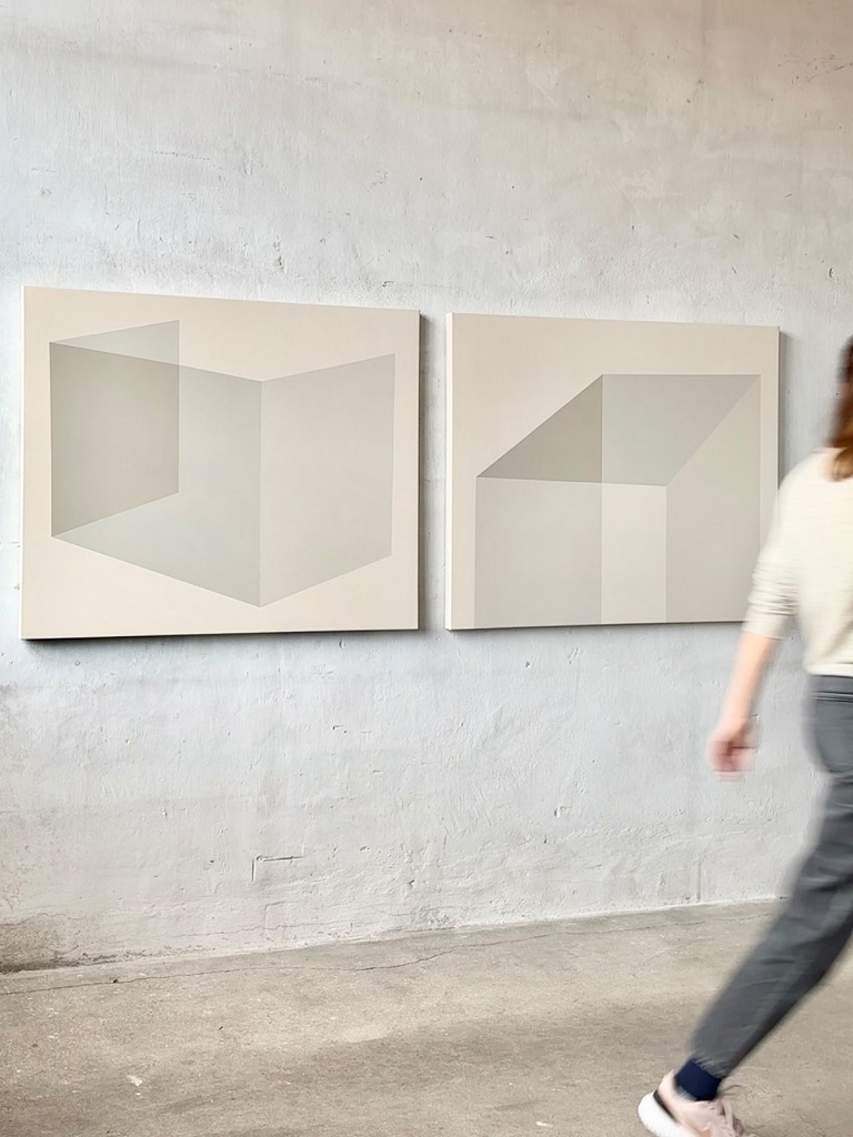 Ein minimalistischer Galerieraum mit zwei abstrakten Gemälden in neutralen Farbtönen. Eine Person in Bewegung passiert die Kunstwerke, wodurch Dynamik im Kontrast zur ruhigen Ästhetik der Bilder entsteht.