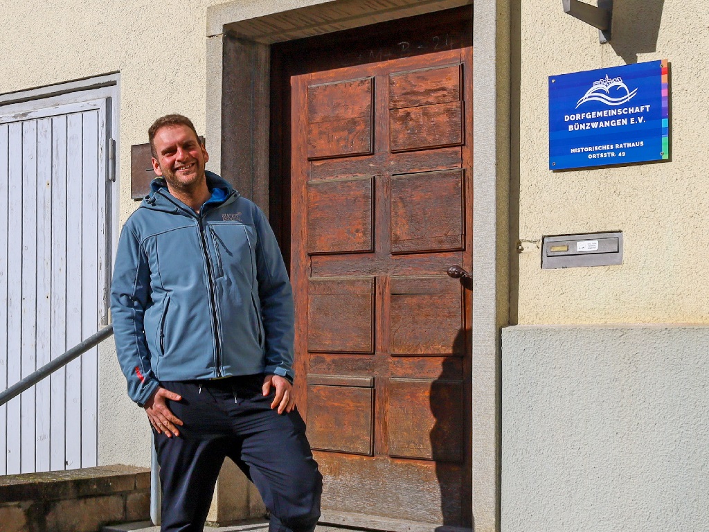 Kevin Reyer, der Vorsitzende der Dorfgemeinschaft Bünzwangen, steht vor dem historischen Rathaus und blickt in die Kamera.