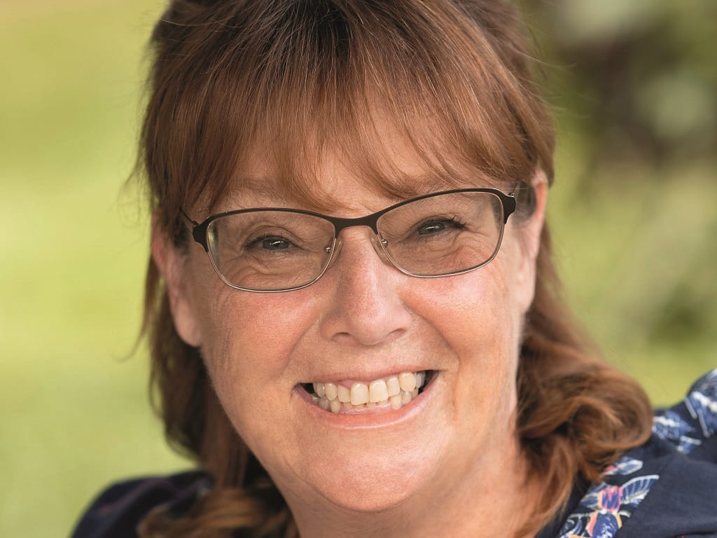 Porträt der Autorin Nicola Förg beim Süßener Kulturfrühling 2026 vor unscharfem grünem Hintergrund im Freien, lächelnd mit braunen Haaren und Brille.