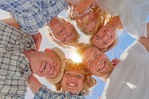 Fröhliche Familie aus mehreren Generationen steht im Kreis und blickt lachend in die Kamera bei Sonnenschein
