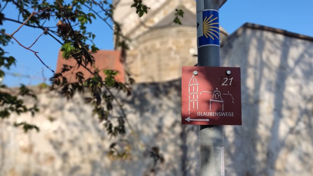 Glaubensweg-Schild an einem Pfosten vor der Stiftskirche in Faurndau – Symbol für das Wandern auf dem Glaubensweg Göppingen.