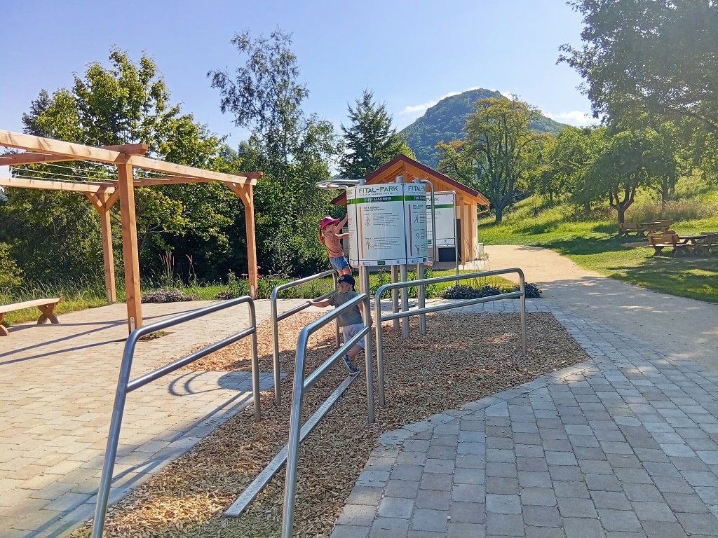 Zwei Kinder erkunden die Bewegungsstation „Die 5 Esslinger“ im FiTal-Park Bad Ditzenbach bei Sonnenschein.