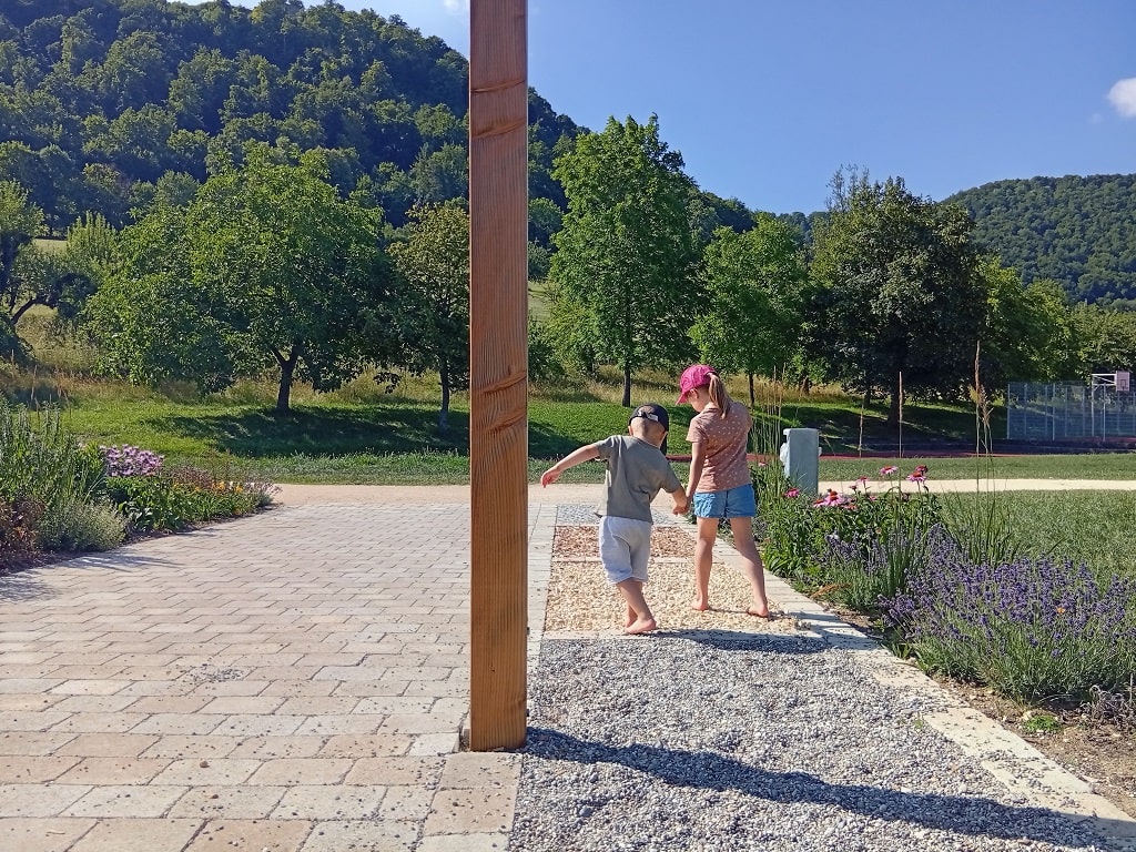 Zwei Kinder laufen barfuß über den Barfußpfad im FiTal-Park Bad Ditzenbach und entdecken verschiedene Untergründe.