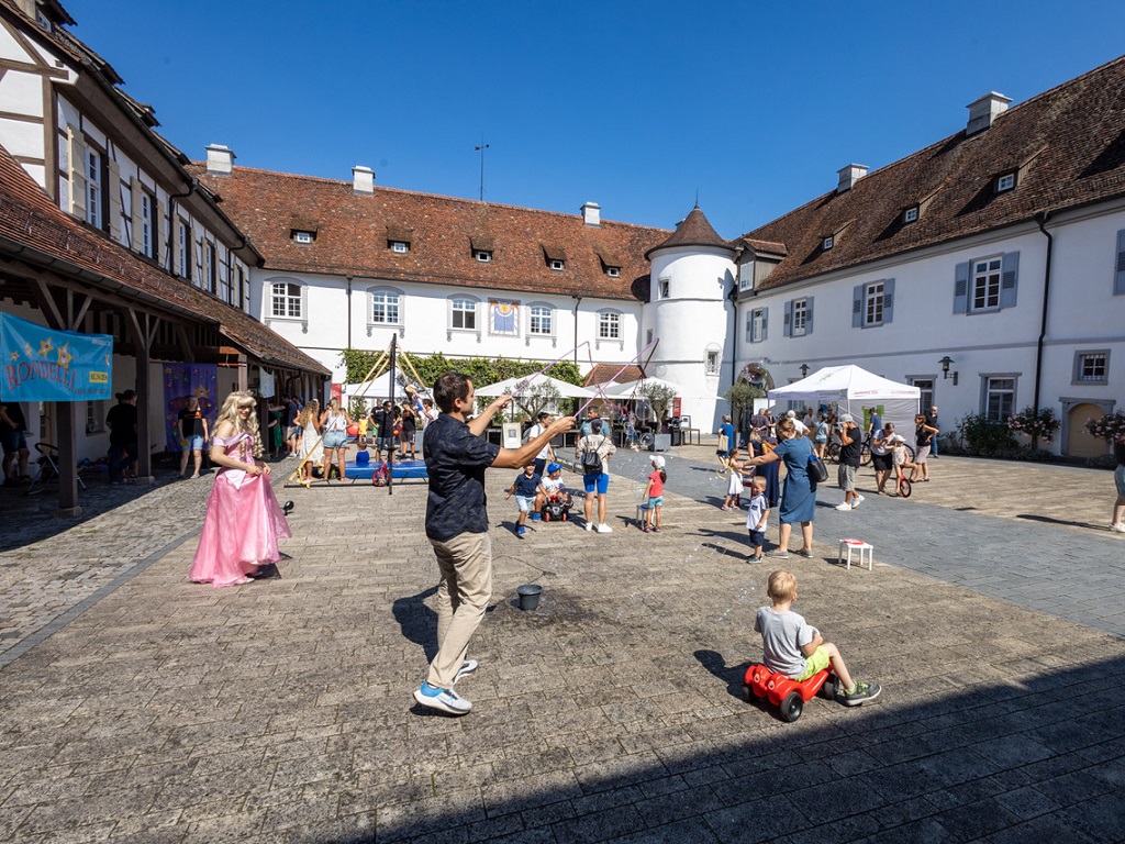 Familien mit Kindern beim Mitmachprogramm im Schlosshof von Schloss Filseck bei sommerlichem Wetter.