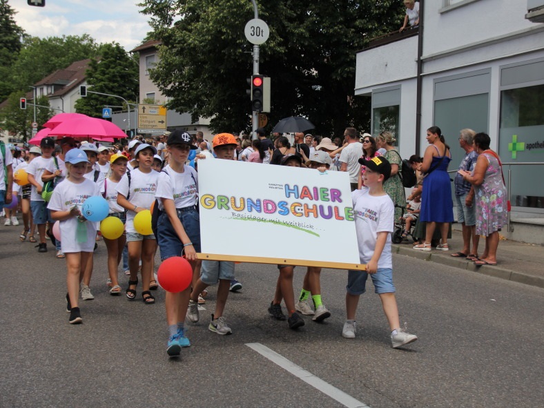 Kinder der Haier Grundschule beim Festumzug 2023 mit buntem Schild und Luftballons.