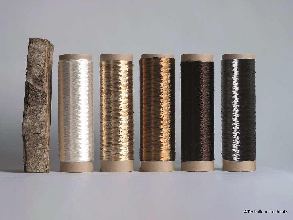 Entwicklung von Carbonfasern aus Buchenholz: fünf Spulen WDBSD CF® in verschiedenen Farbstufen neben einem Holzstück.