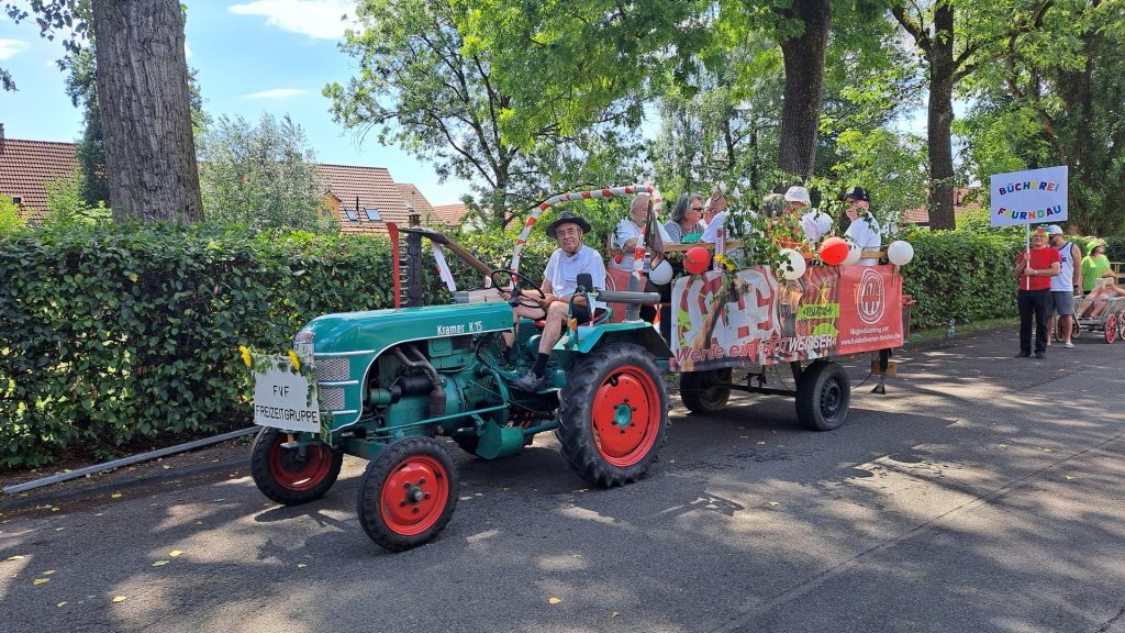 1150 Jahre Faurndau: Festumzugswagen der FVF Freizeitgruppe mit geschmücktem Anhänger beim Festzug 2023. Dahinter Teilnehmer der Bücherei Faurndau mit farbenfrohem Schild.