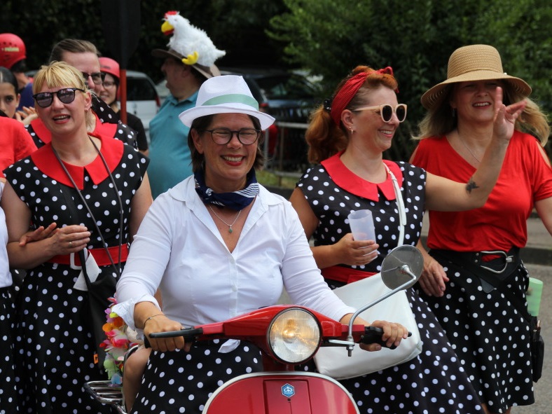 Frauen in 50er-Jahre-Kostümen und eine Frau auf einem roten Roller beim Festumzug des Turnvereins Faurndau 2023, alle fröhlich lachend.