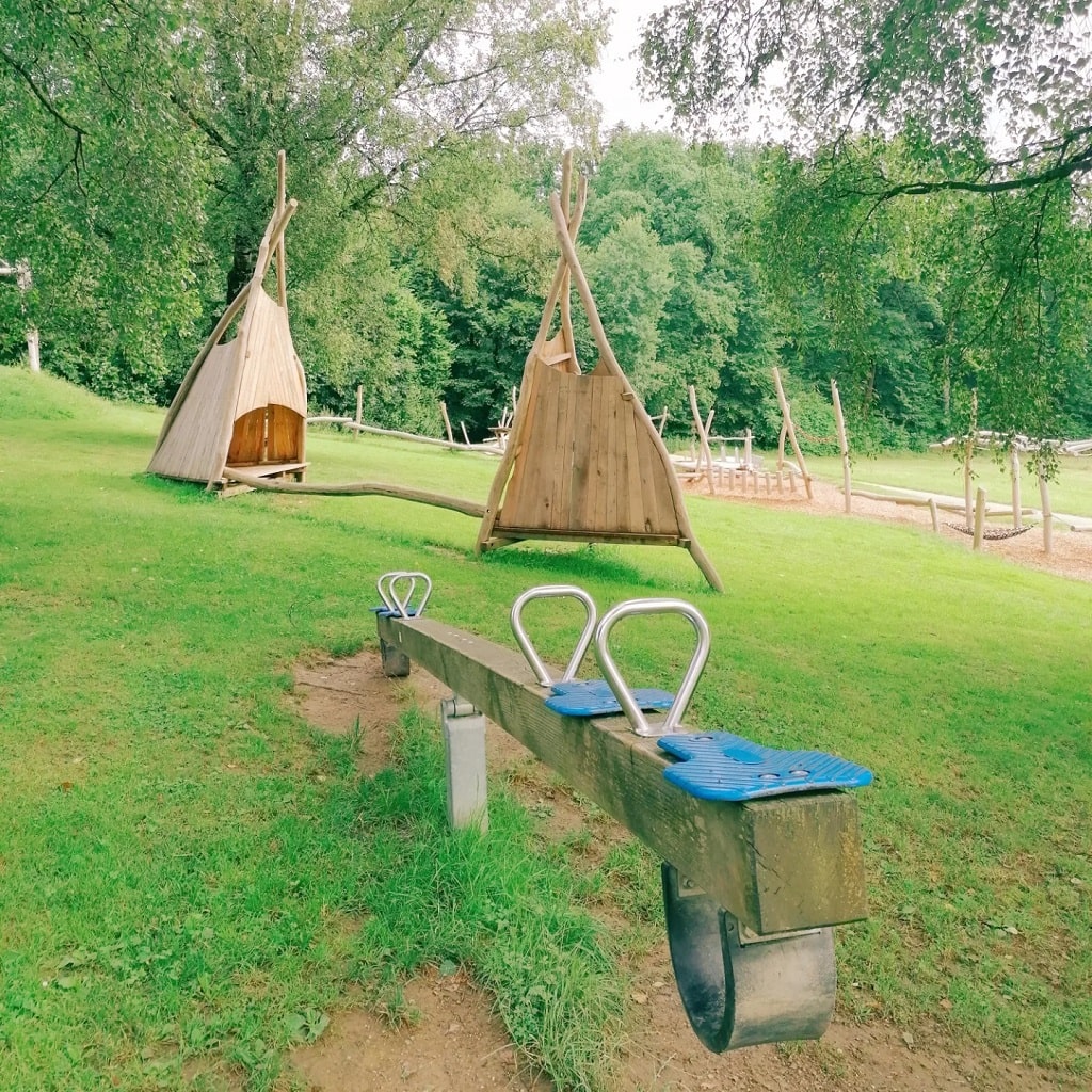 Schattiger Spielbereich mit Wippe und Holz-Zelten beim Waldspielplatz in Wäschenbeuren – ideal für Familien.