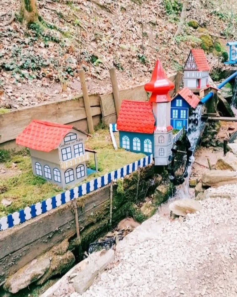 Detailaufnahme eines liebevoll gestalteten Wasserspiels der Schelmenklingen in Lorch. Bunte Miniaturhäuser mit einem roten Turm und einem Wasserrad, das vom klaren Bach angetrieben wird.