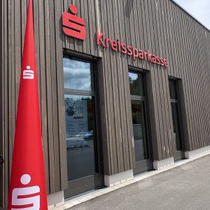 Außenansicht der Kreissparkassen-Filiale in Wäschenbeuren mit rotem Sparkassen-Logo und großem Werbeaufsteller in Form eines Kegels vor dem Eingang.