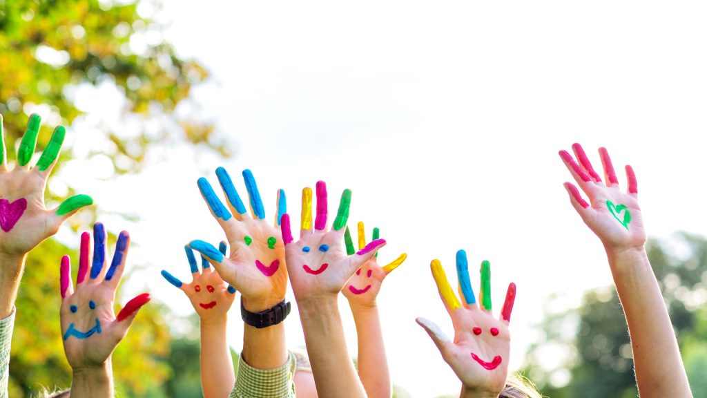 Titelbild Schülerferienprogramm Süßen 2025: Kinderhände mit bunten Farben bemalt, in die Luft gestreckt, jede Hand zeigt ein fröhliches Gesicht – ein kreativer Sommermoment voller Spaß und Farbe.