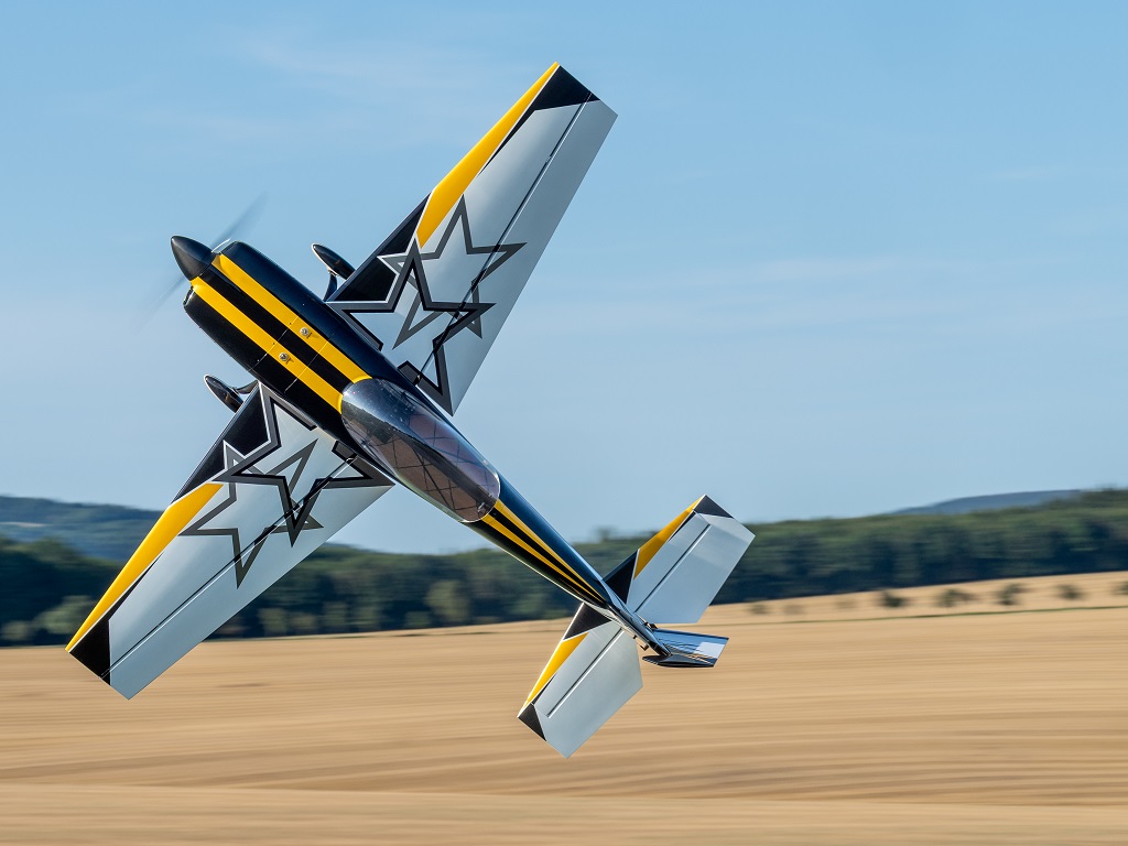 Samstagsprogramm der Flugtage Donzdorf 2025: Ein Modellflugzeug in Schwarz-Gelb mit Stern-Design zeigt eine rasante Flugfigur. Knapp über einem Feld und vor blauem Himmel.