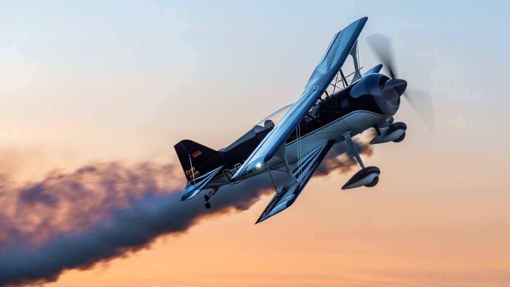 Ein schwarz-weiß lackierter Doppeldecker vom Typ Pitts S-2B zieht eine Rauchspur durch den Himmel im Abendlicht – dynamisch eingefangen im Kunstflug. Zu sehen bei den Flugtagen 2025 in Donzdorf.