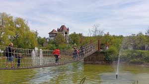 Hängebrücke in Tripsdrill – Besucher überqueren eine Seilbrücke über einen Teich mit Springbrunnen, im Hintergrund das Schloss.