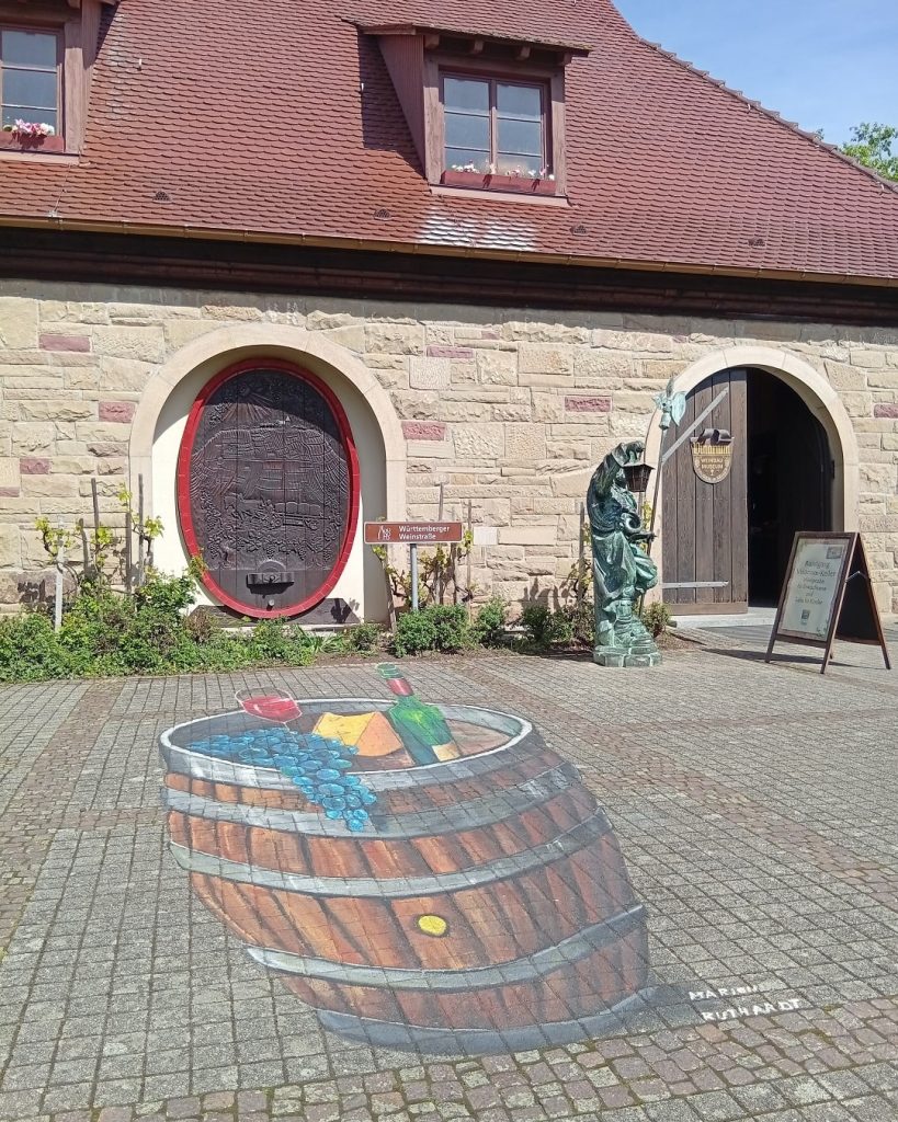 Weinbaumuseum im Erlebnispark Tripsdrill – Eingangsbereich mit Wandrelief, Statue und 3D-Straßenmalerei eines Weinfasses.