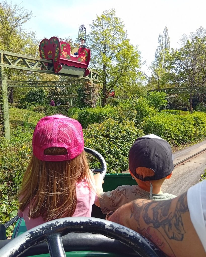 Familienfahrt im Erlebnispark Tripsdrill – Zwei Kinder steuern ein nostalgisches Auto durch die grüne Parklandschaft.