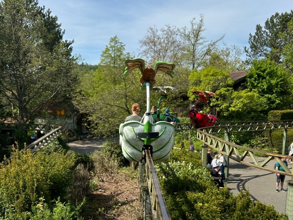 Familienattraktion im Erlebnispark Tripsdrill – Kinder fahren in blütenförmigen Gondeln auf einer Hochbahn durch die Natur.