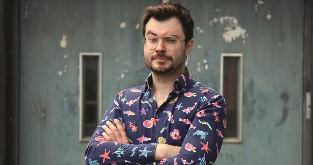 Sebastian Klussmann, Quiz-Champion aus „Gefragt – Gejagt“, mit verschränkten Armen im bunten Hemd