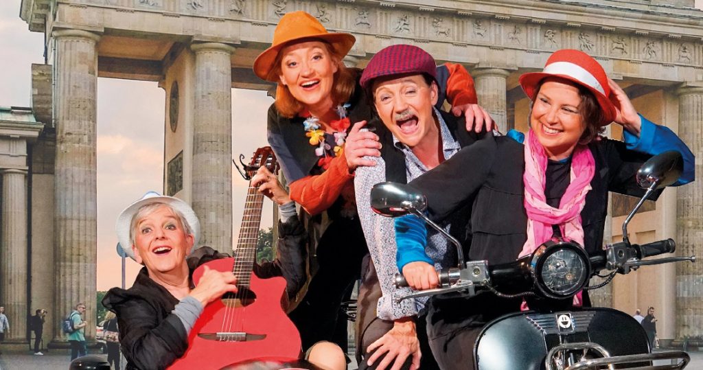 Vier Darstellerinnen mit Gitarre und Motorroller vor dem Brandenburger Tor – Musiktheater „50 Jahr blondes Haar“ über Politik und Schlager.
